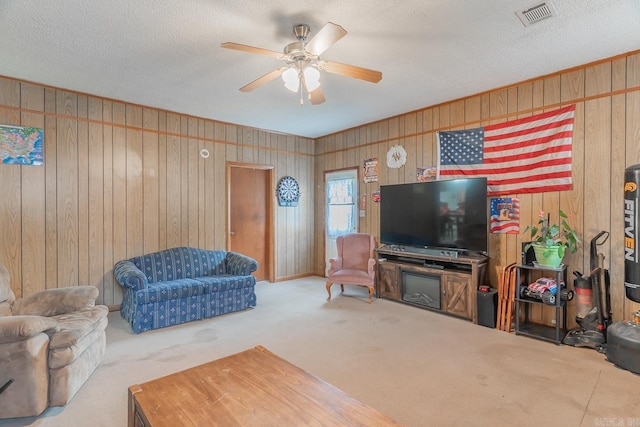 carpeted living room featuring a textured ceiling, wooden walls, visible vents, and a ceiling fan