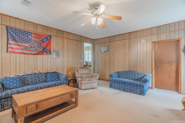 living room with wood walls, carpet flooring, visible vents, and a ceiling fan