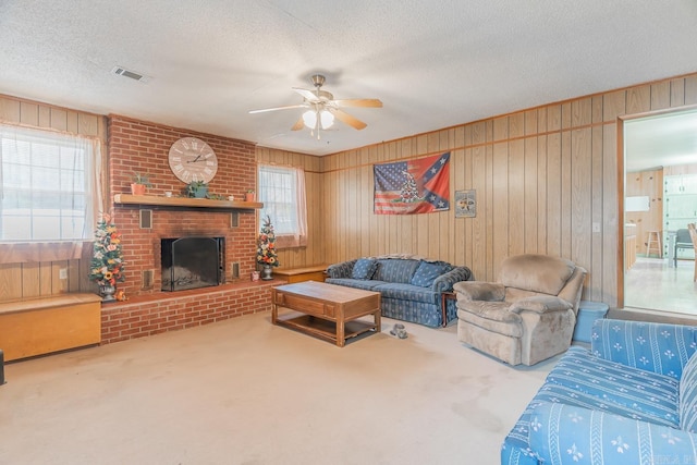 carpeted living area with a fireplace, visible vents, a ceiling fan, a textured ceiling, and wooden walls