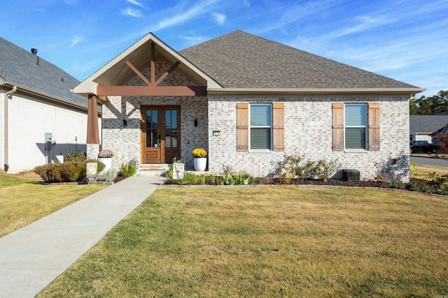 view of front of home with a front yard, roof with shingles, and brick siding
