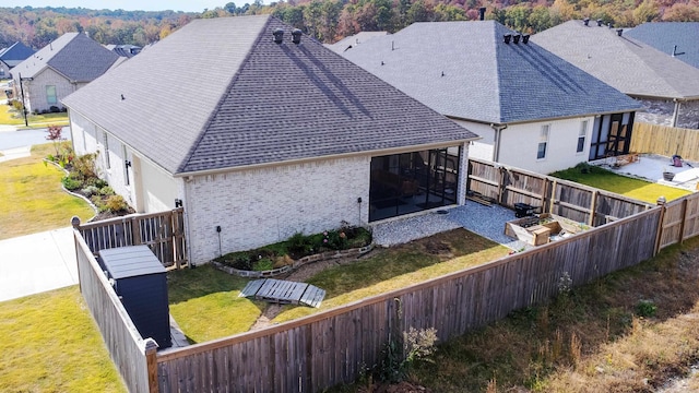 back of house featuring a yard, a shingled roof, brick siding, and a fenced backyard