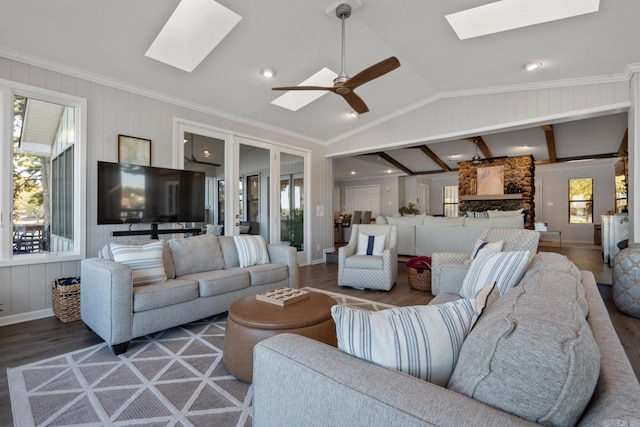 living room with a stone fireplace, dark hardwood / wood-style floors, crown molding, lofted ceiling with skylight, and ceiling fan