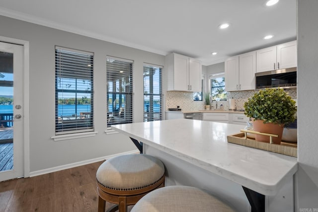 kitchen featuring white cabinets, dark hardwood / wood-style flooring, appliances with stainless steel finishes, a breakfast bar area, and a water view