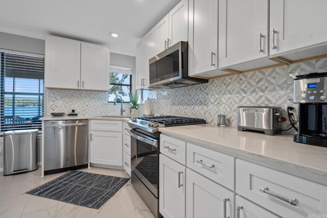 kitchen featuring stainless steel appliances, sink, white cabinets, light stone counters, and tasteful backsplash