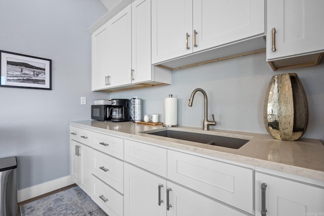 kitchen featuring light stone counters, sink, and white cabinets