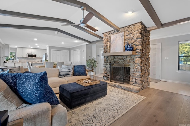 living room with vaulted ceiling with beams, light hardwood / wood-style flooring, a fireplace, and crown molding