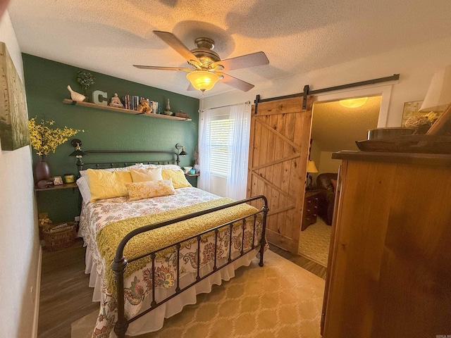 bedroom with hardwood / wood-style floors, a barn door, a textured ceiling, and ceiling fan