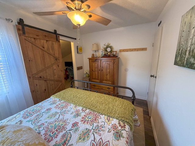 bedroom with ceiling fan, a textured ceiling, a barn door, and hardwood / wood-style floors