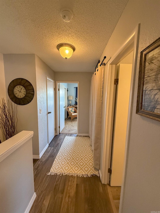 corridor with a textured ceiling and hardwood / wood-style flooring