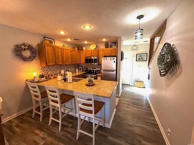 kitchen featuring a textured ceiling, kitchen peninsula, hanging light fixtures, stainless steel appliances, and decorative backsplash