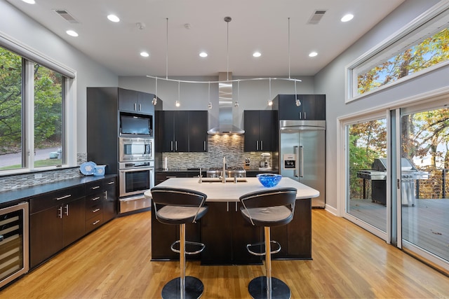 kitchen with wall chimney range hood, pendant lighting, beverage cooler, stainless steel built in fridge, and a breakfast bar area