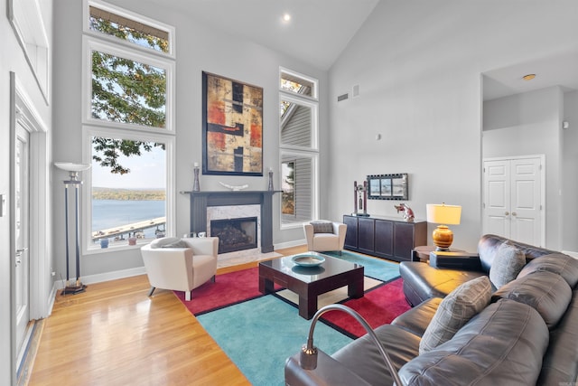 living room featuring a water view, high vaulted ceiling, a wealth of natural light, and light wood-type flooring