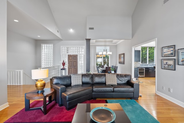 living room featuring wine cooler, a chandelier, high vaulted ceiling, light wood-type flooring, and ornate columns