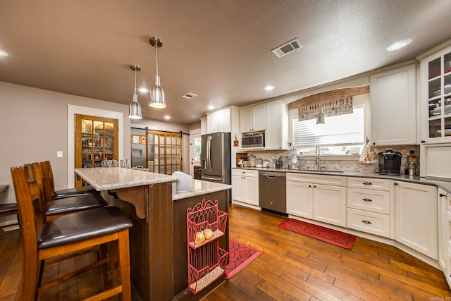 kitchen with appliances with stainless steel finishes, a barn door, dark wood-type flooring, sink, and a center island