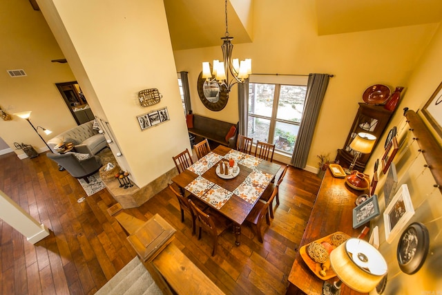 dining area with a towering ceiling, a chandelier, and dark wood-type flooring