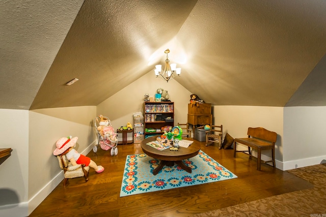 playroom featuring a notable chandelier, a textured ceiling, vaulted ceiling, and dark hardwood / wood-style floors