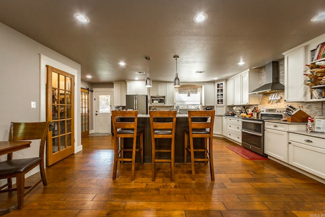 kitchen with a barn door, a center island, hanging light fixtures, stainless steel appliances, and wall chimney exhaust hood