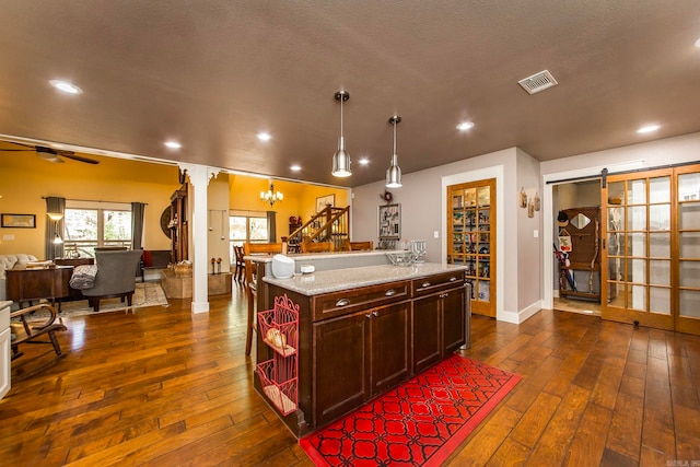 kitchen with an island with sink, hanging light fixtures, dark hardwood / wood-style floors, and ornate columns