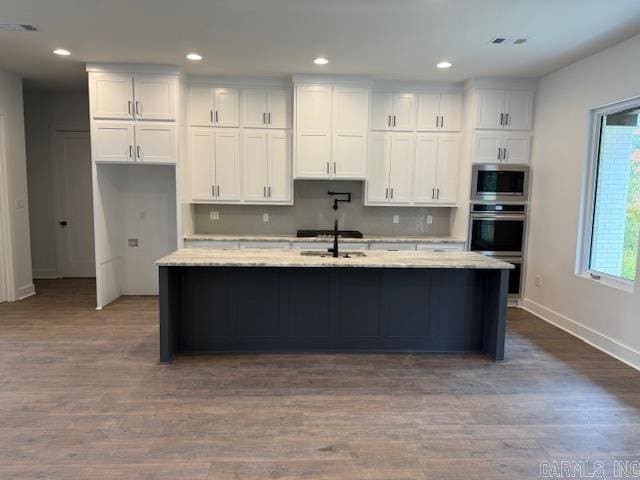 kitchen featuring stainless steel microwave, white cabinetry, and a center island with sink