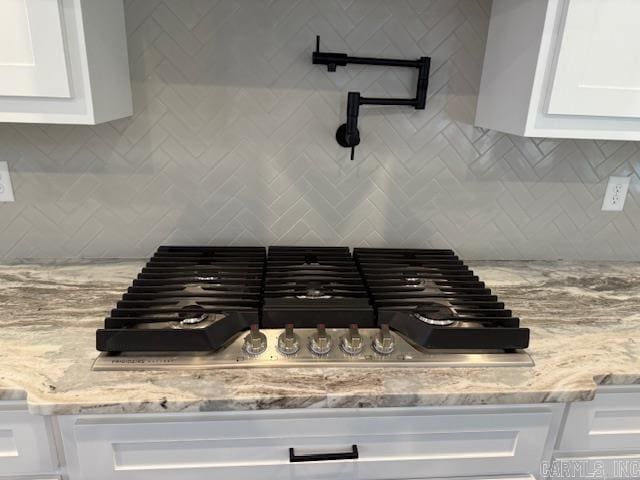 interior details featuring stainless steel gas cooktop, light stone countertops, backsplash, and white cabinets