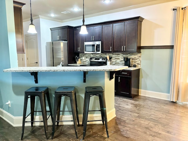 kitchen featuring a breakfast bar area, hardwood / wood-style floors, decorative light fixtures, appliances with stainless steel finishes, and light stone counters