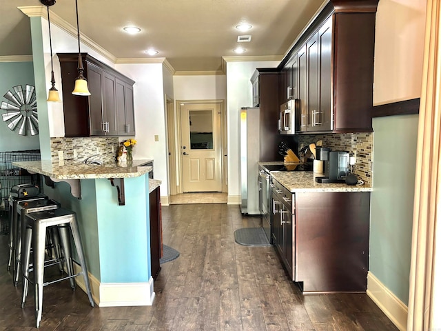 kitchen with light stone counters, dark hardwood / wood-style flooring, appliances with stainless steel finishes, a breakfast bar area, and decorative light fixtures