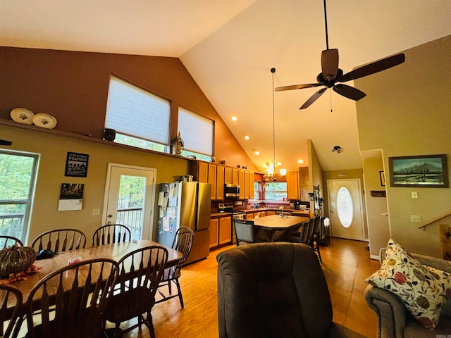 dining area featuring high vaulted ceiling, ceiling fan with notable chandelier, light wood-type flooring, and a wealth of natural light