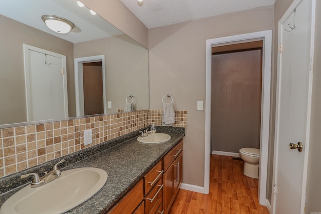 bathroom featuring hardwood / wood-style flooring, toilet, vanity, a textured ceiling, and tasteful backsplash