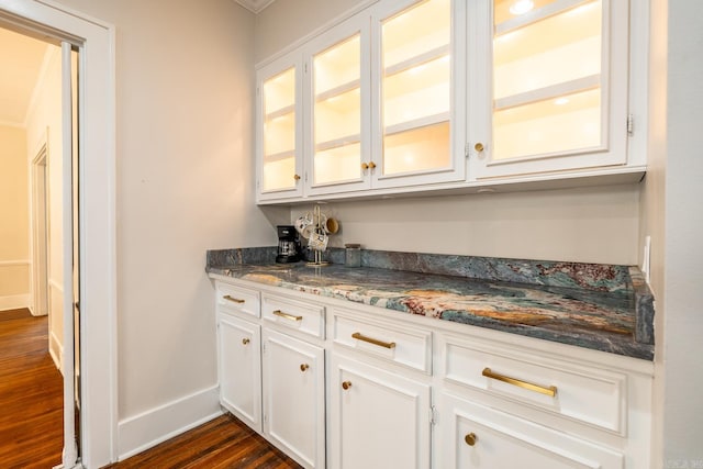 bar featuring dark stone countertops, ornamental molding, dark hardwood / wood-style floors, and white cabinets