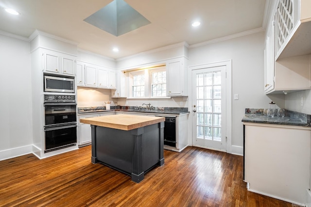 kitchen with dark wood-type flooring, black appliances, a center island, white cabinets, and butcher block countertops