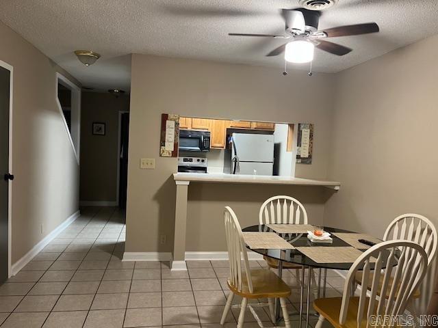 dining area featuring a ceiling fan, a textured ceiling, baseboards, and light tile patterned floors