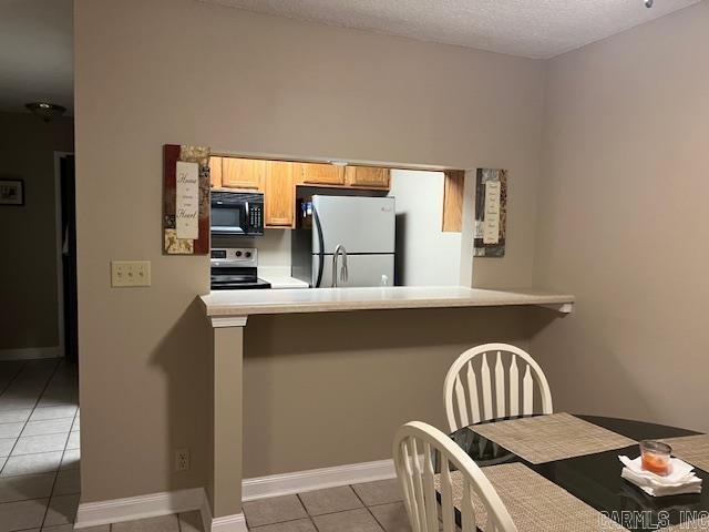 kitchen with electric range, tile patterned floors, a peninsula, freestanding refrigerator, and black microwave