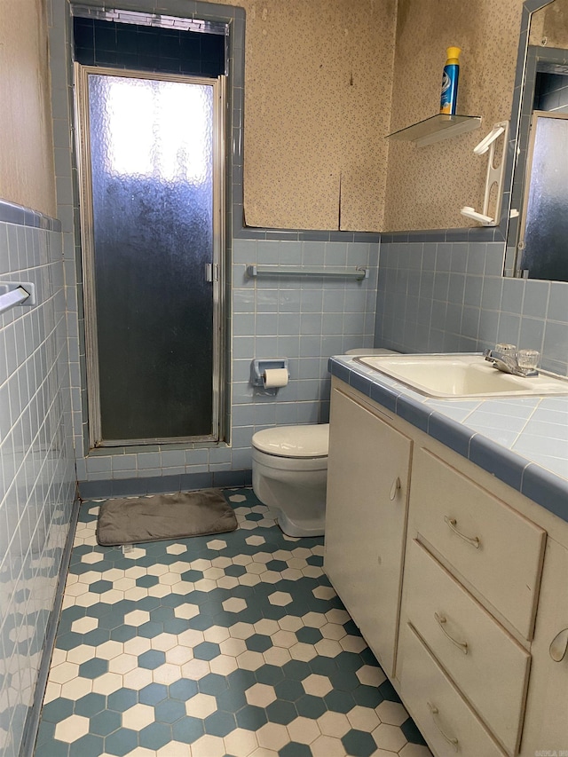 bathroom with vanity, toilet, tile walls, and a shower with shower door