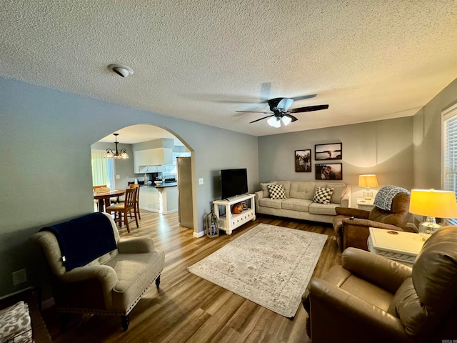 living room with ceiling fan with notable chandelier, a textured ceiling, and light hardwood / wood-style floors