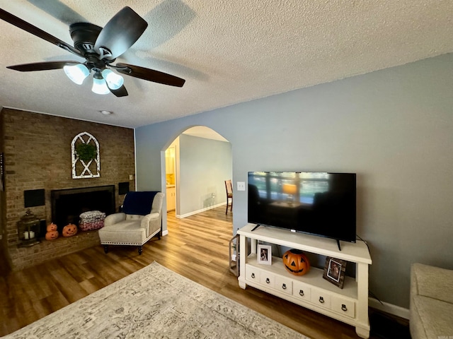 living room with ceiling fan, hardwood / wood-style flooring, a textured ceiling, and a brick fireplace