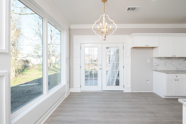 unfurnished dining area with an inviting chandelier, plenty of natural light, ornamental molding, and french doors