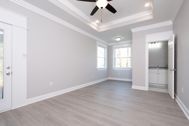 unfurnished bedroom featuring sink, ceiling fan, a tray ceiling, ornamental molding, and light hardwood / wood-style floors