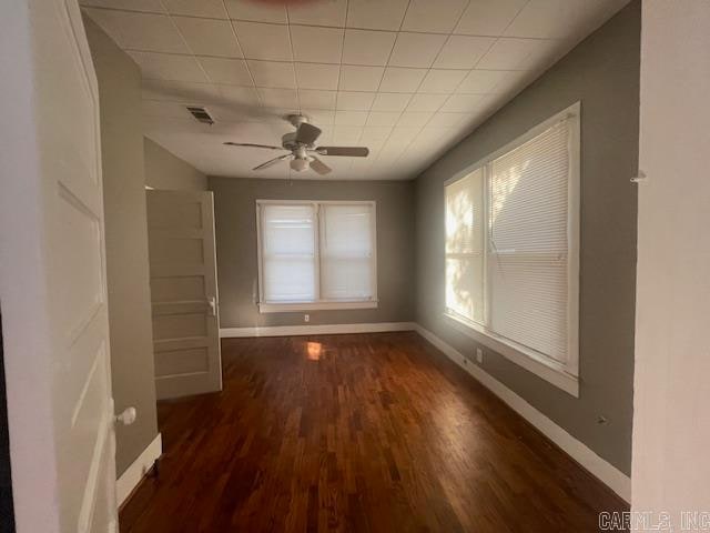 unfurnished dining area with dark wood-type flooring, a paneled ceiling, a healthy amount of sunlight, and ceiling fan