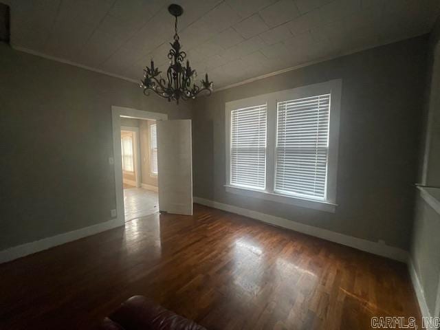 empty room with dark wood-type flooring, crown molding, and a chandelier