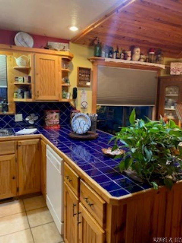 interior space with open shelves, dishwasher, tile countertops, light tile patterned floors, and backsplash