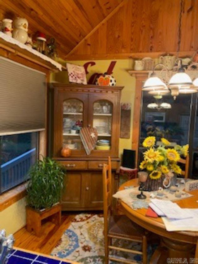dining space featuring wood finished floors, wood walls, lofted ceiling, and wooden ceiling