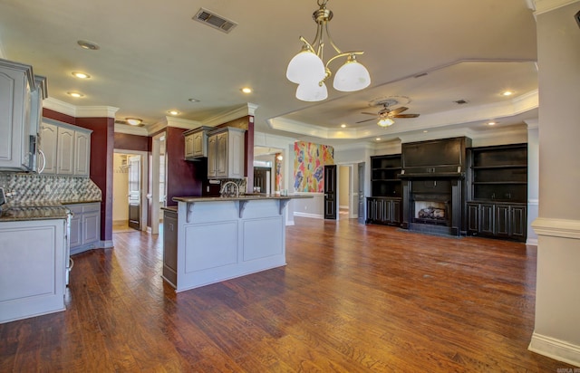 kitchen with ceiling fan with notable chandelier, backsplash, a tray ceiling, pendant lighting, and dark wood-type flooring