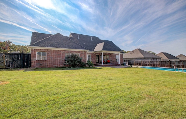 rear view of property with a fenced in pool, a patio area, and a lawn