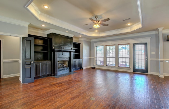 unfurnished living room featuring dark wood-type flooring, crown molding, a tray ceiling, and ceiling fan