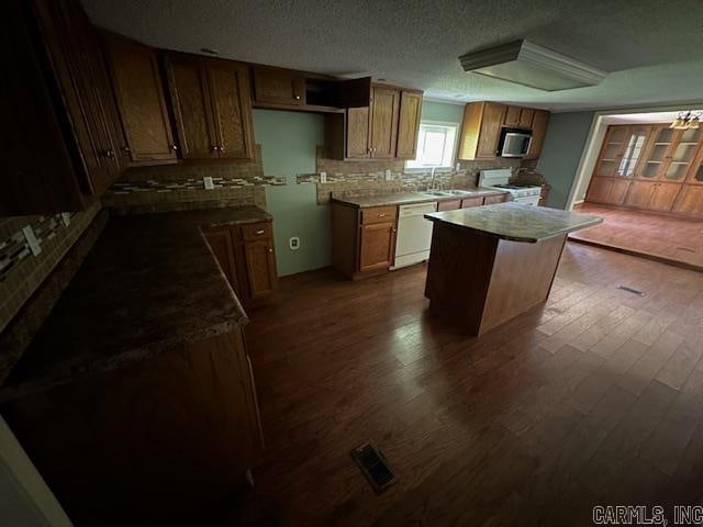 kitchen with white appliances, a kitchen island, backsplash, a textured ceiling, and dark hardwood / wood-style floors