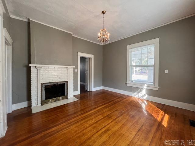 919 E Hamilton Ave, Wynne, AR 72396 - unfurnished living room with crown molding, baseboards, an inviting chandelier, and wood finished floors