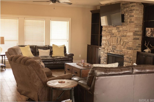 living room with ceiling fan, a stone fireplace, ornamental molding, and hardwood / wood-style floors