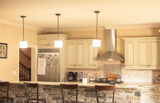 kitchen with wall chimney range hood, stainless steel appliances, a kitchen bar, and light stone counters