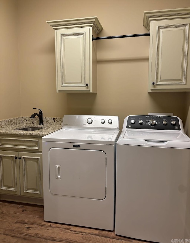 clothes washing area featuring cabinets, sink, washing machine and clothes dryer, and dark hardwood / wood-style flooring