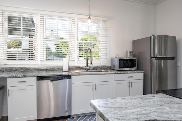 kitchen with white cabinets, appliances with stainless steel finishes, light stone countertops, pendant lighting, and sink